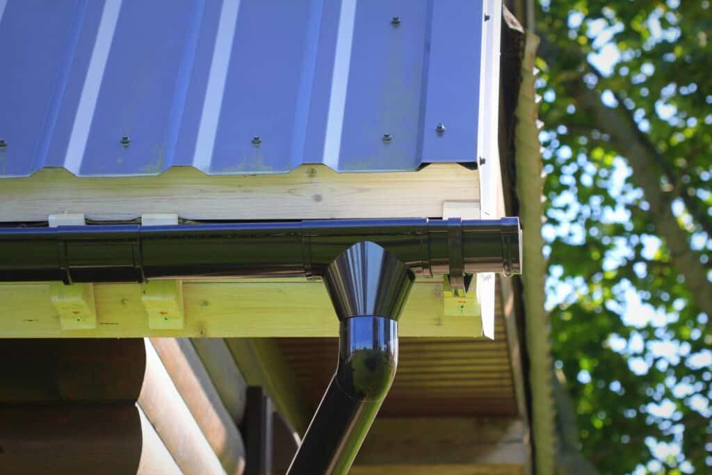 Roof gutter pipeline system on corner of house. Building rain gutter with holders and downspout pipe against the sky.